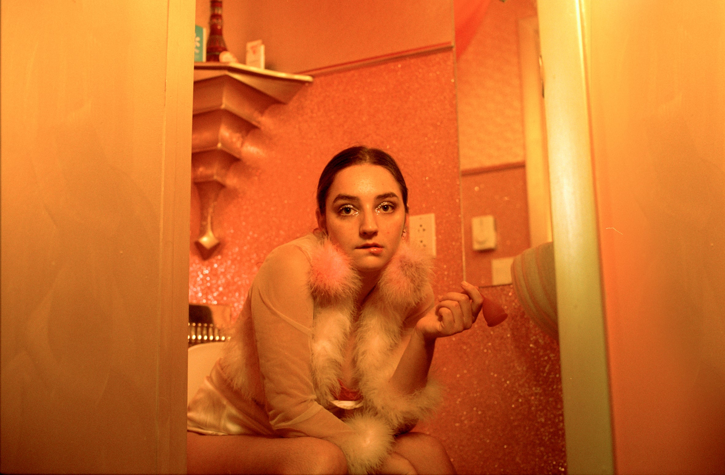 Photograph of a young lady sitting on the toilet, holding a menstrual cup in her left hand.