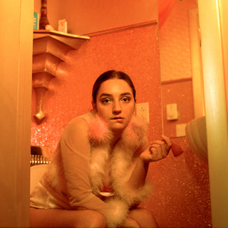 Photograph of a young lady sitting on the toilet, holding a menstrual cup in her left hand.