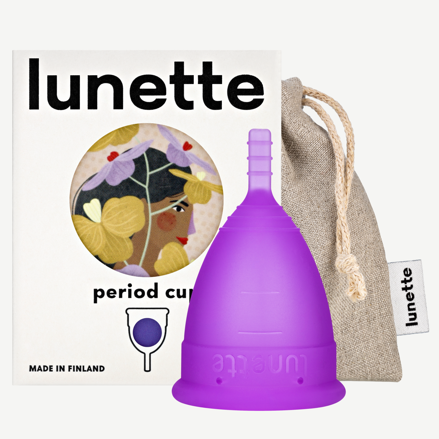 A purple Lunette period cup displayed alongside its packaging box with a floral design and a linen storage pouch. The box includes the text 'period cup', 'made in Finland', and the brand name 'Lunette'.